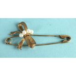 A brooch in the form of a safety pin overlaid with a textured bow and four cultured pearls,