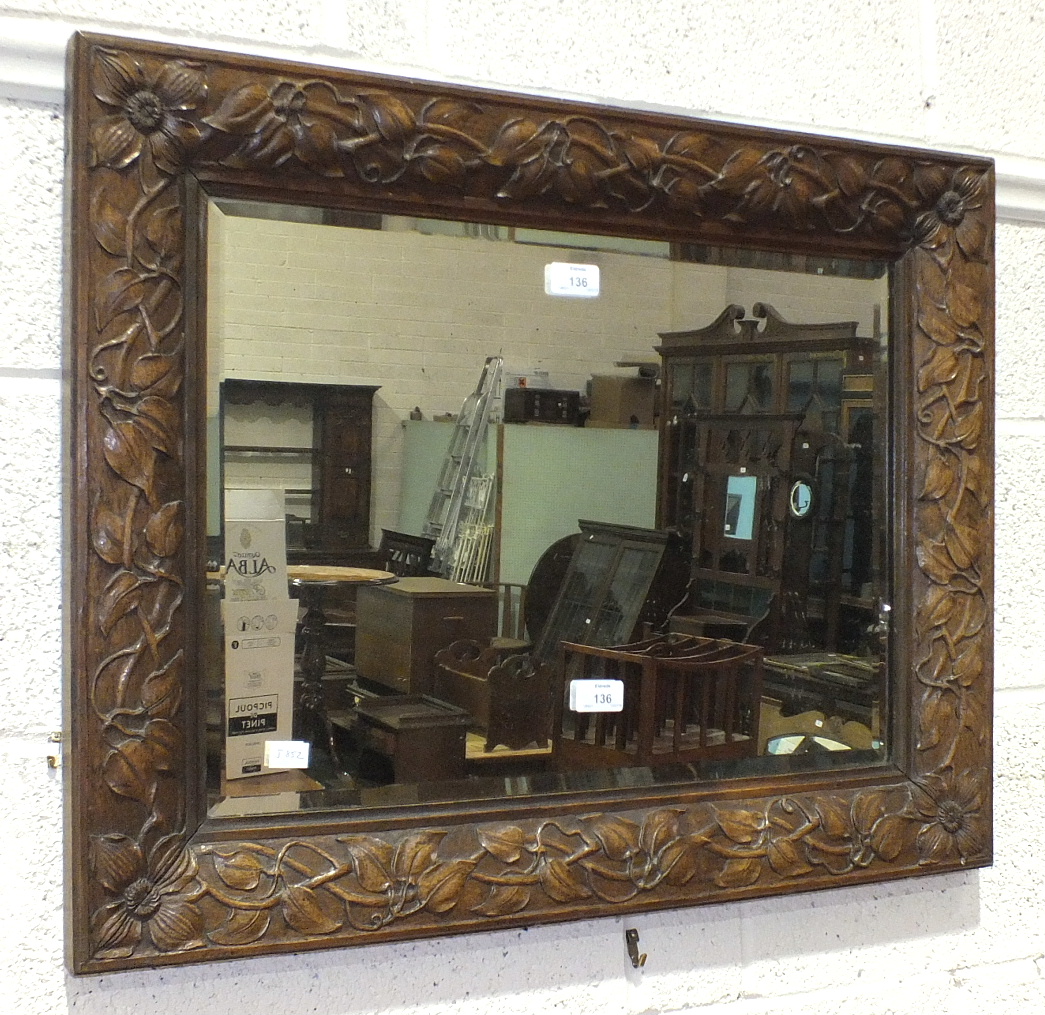 An oak-framed bevelled-edge mirror, the frame carved with flowers in each corner and leaves along