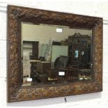 An oak-framed bevelled-edge mirror, the frame carved with flowers in each corner and leaves along