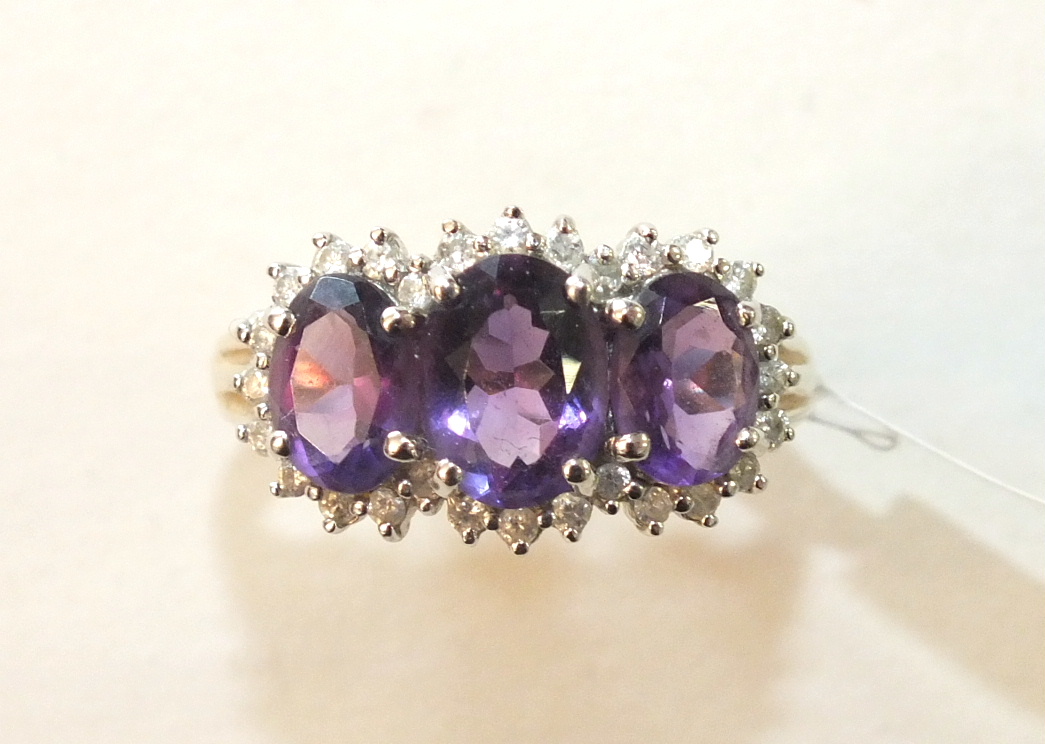 A 9ct gold ring set three amethysts within a surround of diamond points, size P, 3.3g.