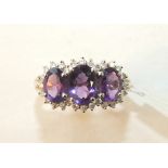 A 9ct gold ring set three amethysts within a surround of diamond points, size P, 3.3g.