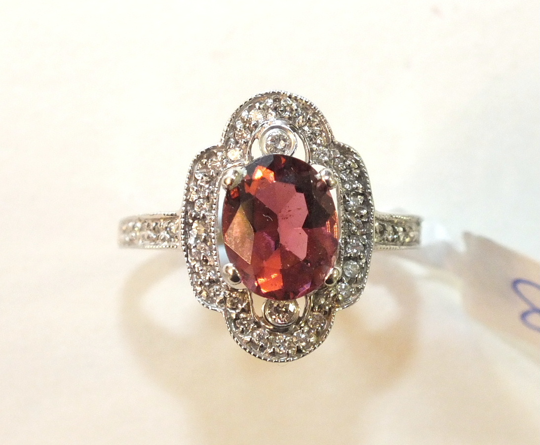 A pink tourmaline and diamond cluster ring claw-set an oval tourmaline between two collet-set