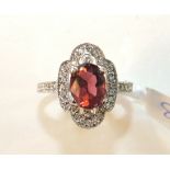 A pink tourmaline and diamond cluster ring claw-set an oval tourmaline between two collet-set