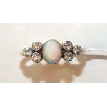 An Edwardian opal and diamond ring millegrain-set an oval opal between triplets of old brilliant-cut