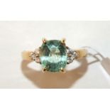 A modern 18ct yellow gold ring claw-set a pale green tourmaline between triplets of brilliant-cut