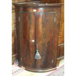 A George III mahogany bow-fronted hanging corner cupboard, the moulded cornice above a pair of