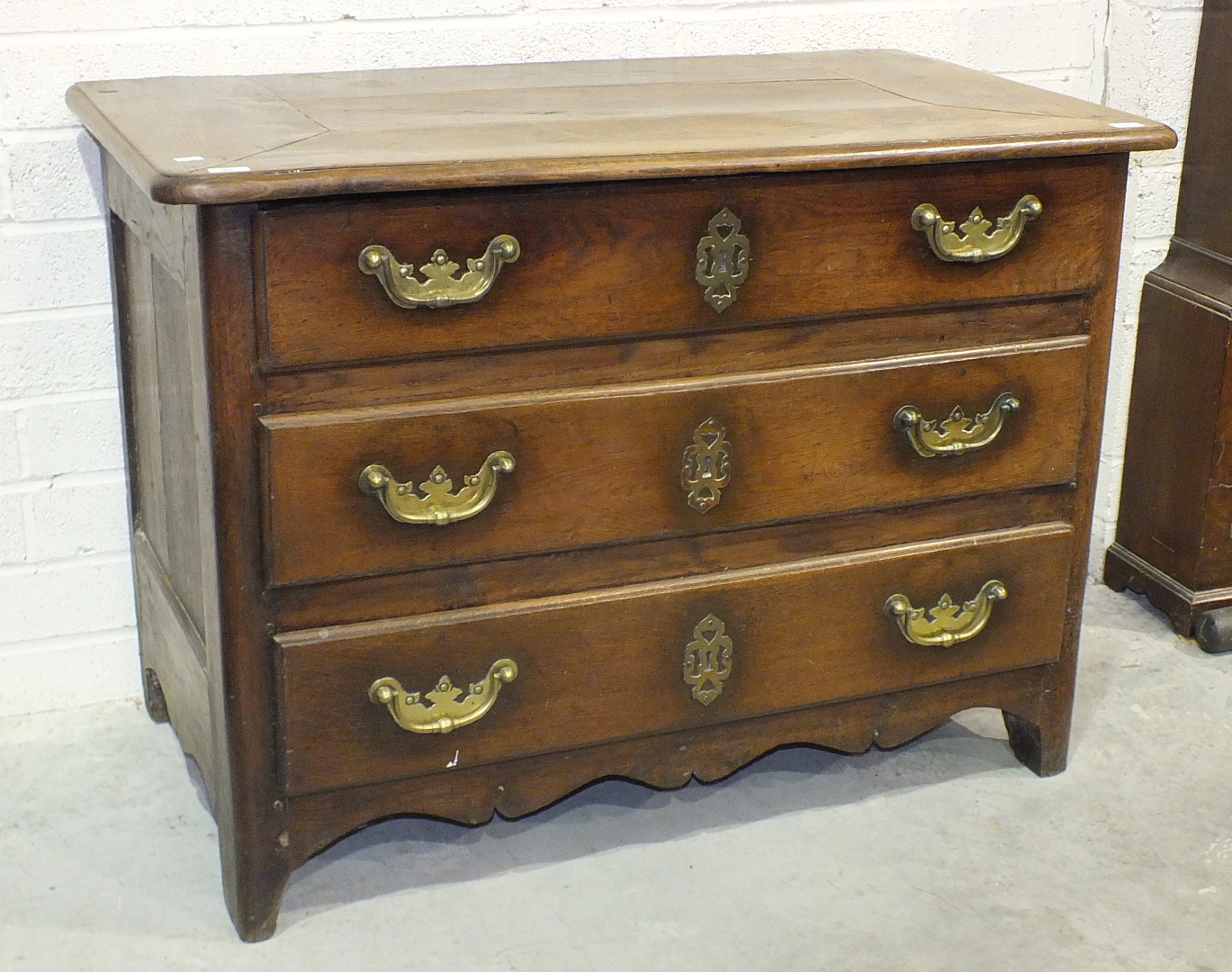 An early-18th century Continental chestnut or oak chest of three long drawers with heavy brass