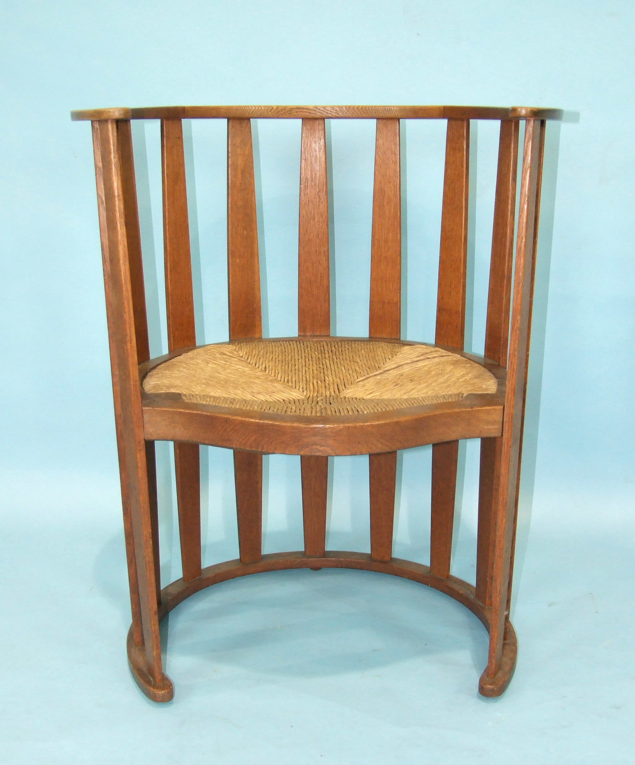 An Arts & Crafts-style oak slatted chair of cylinder shape, with serpentine-fronted drop-in rush