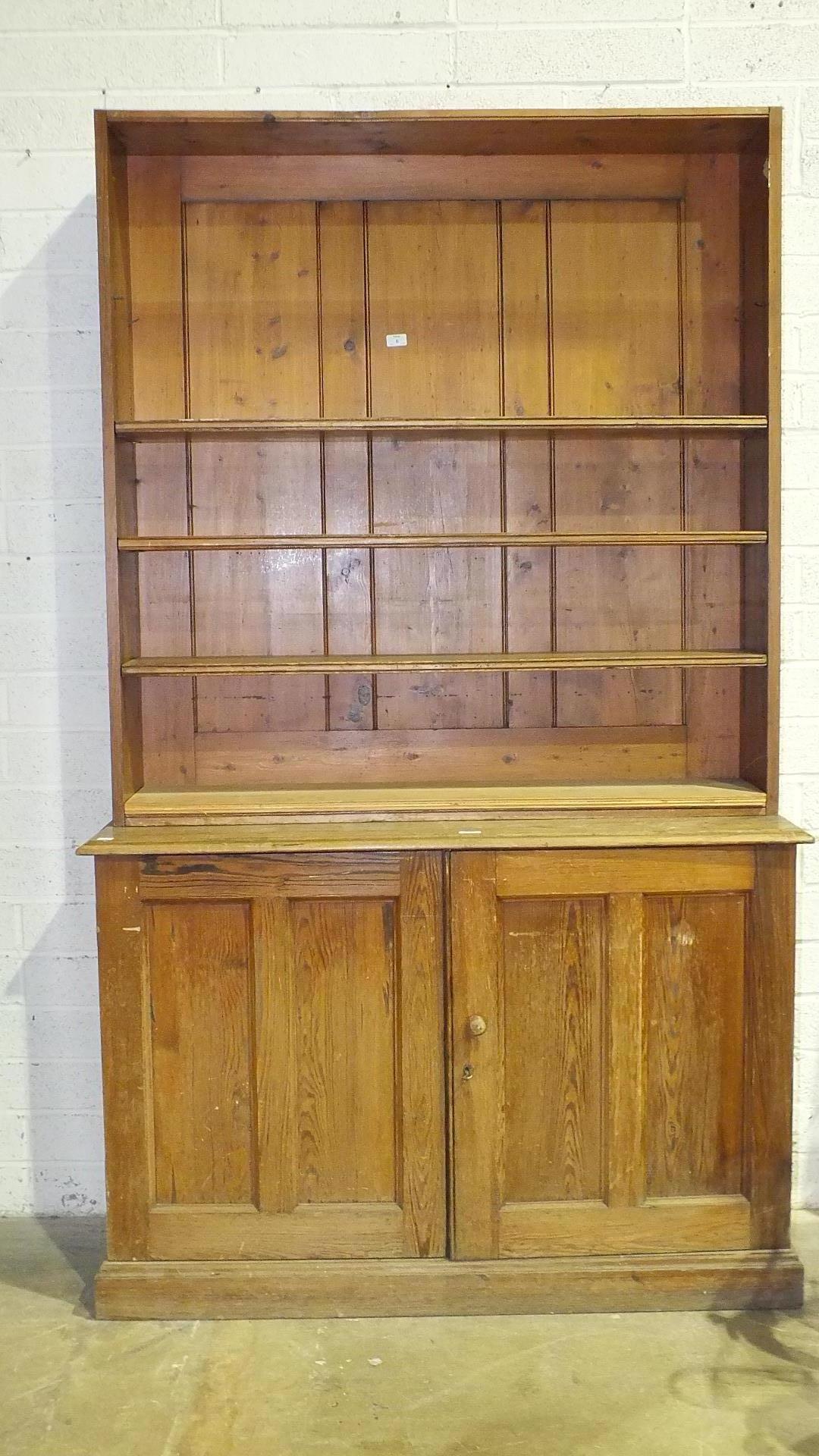 A pitch pine bookcase, the open shelves above a pair of panel doors, 127cm wide, 204cm high, (