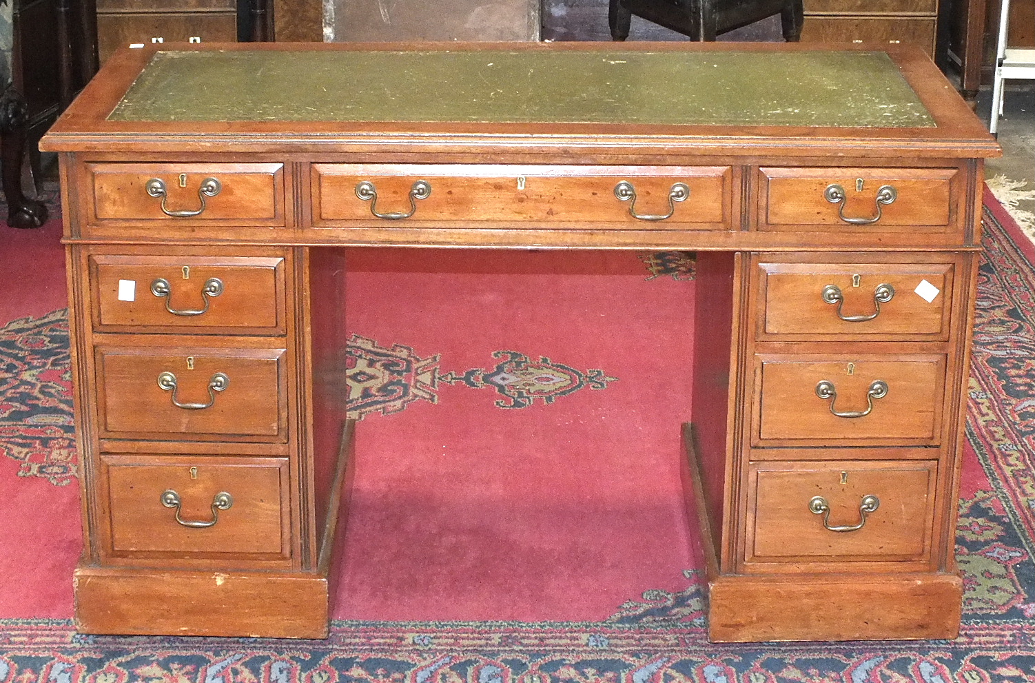 An Edwardian stained mahogany knee-hole desk, the rectangular top with writing inset, and three