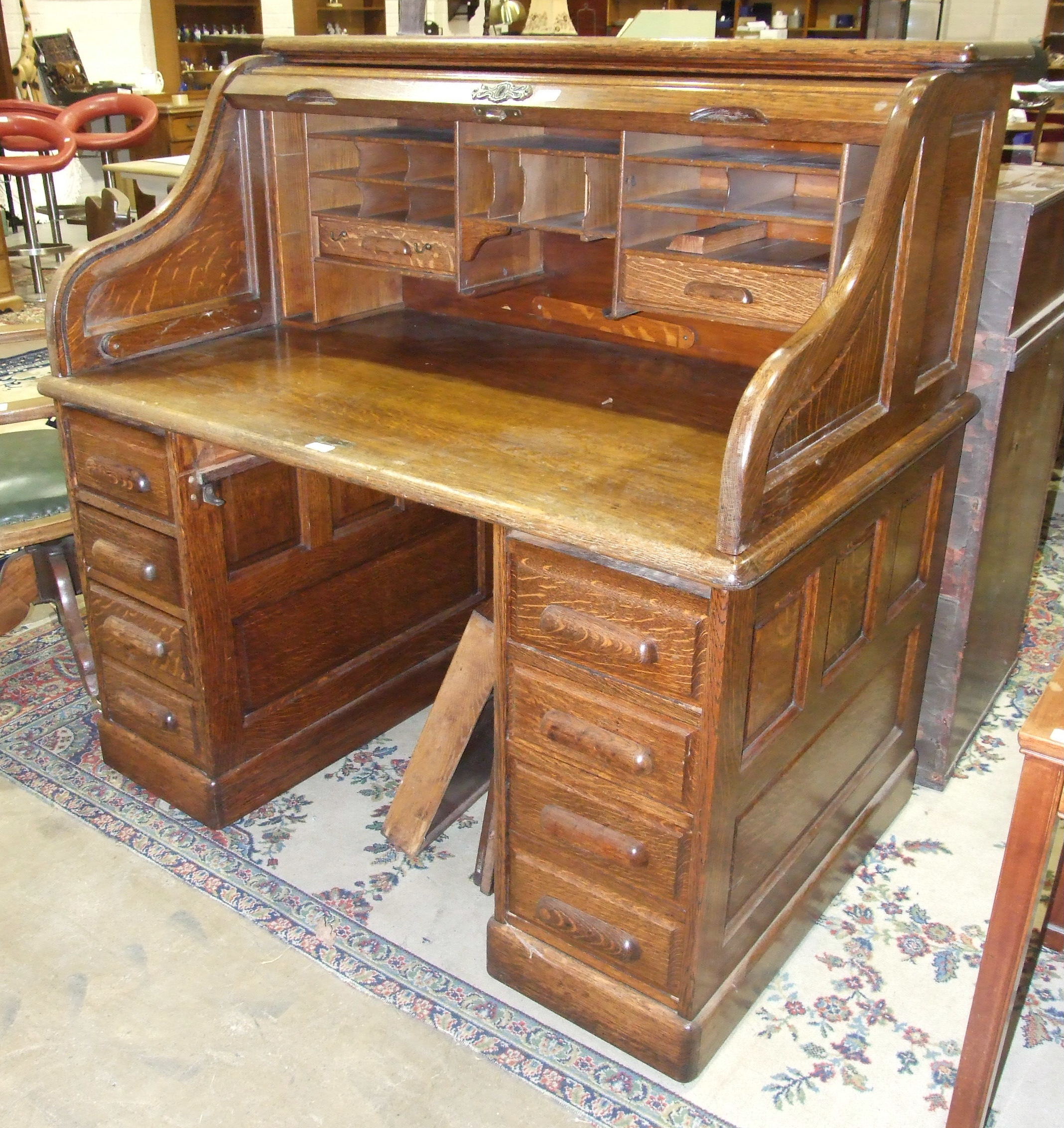 An early-20th century oak roll-top desk, the interior fitted with drawer and pigeon holes over a