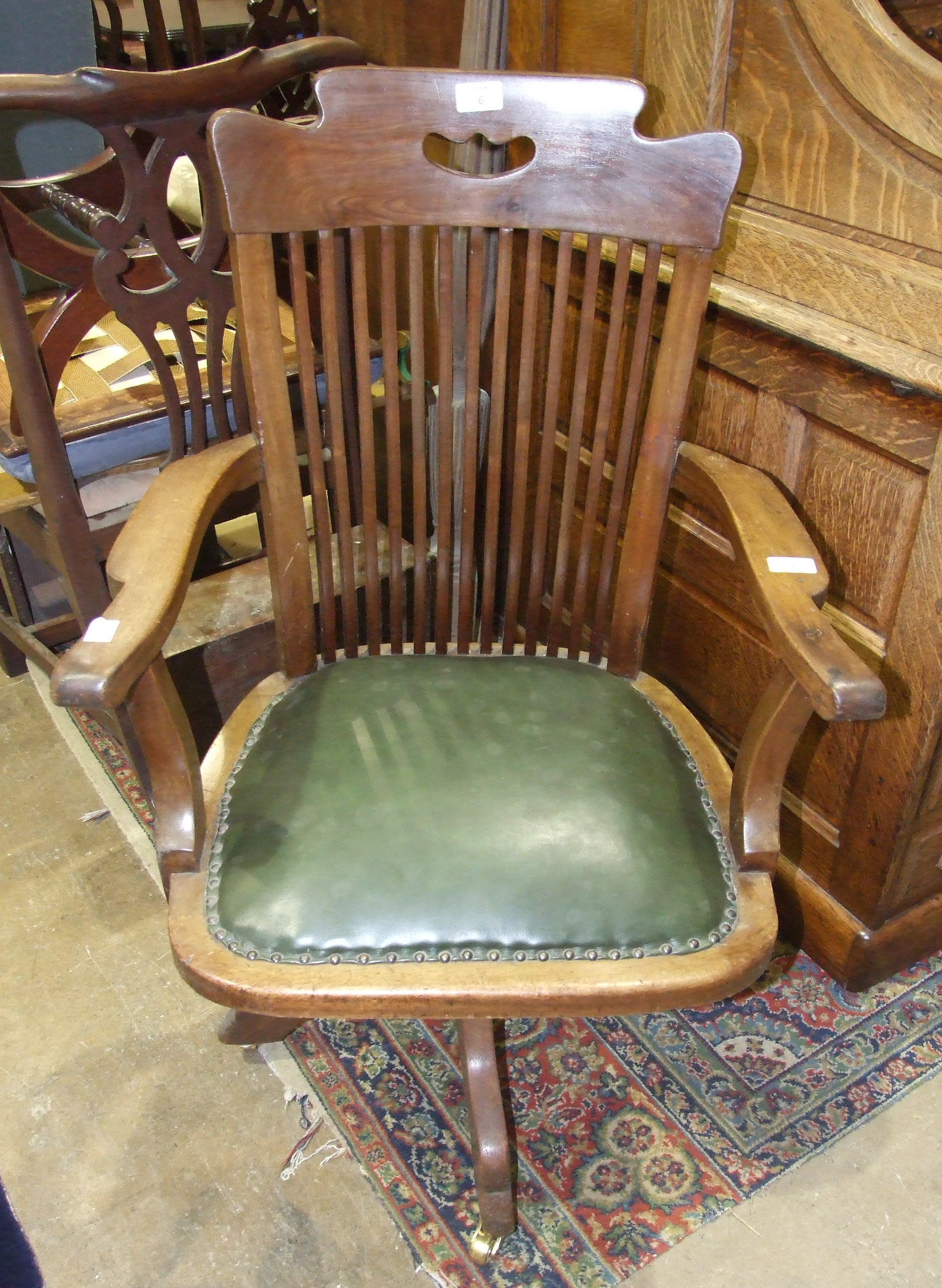 An early-20th century oak office swivel armchair with slatted back and padded seat and quadruped
