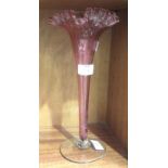 A cranberry glass trumpet-shaped vase with wavy rim, on circular clear glass base, 31cm high.