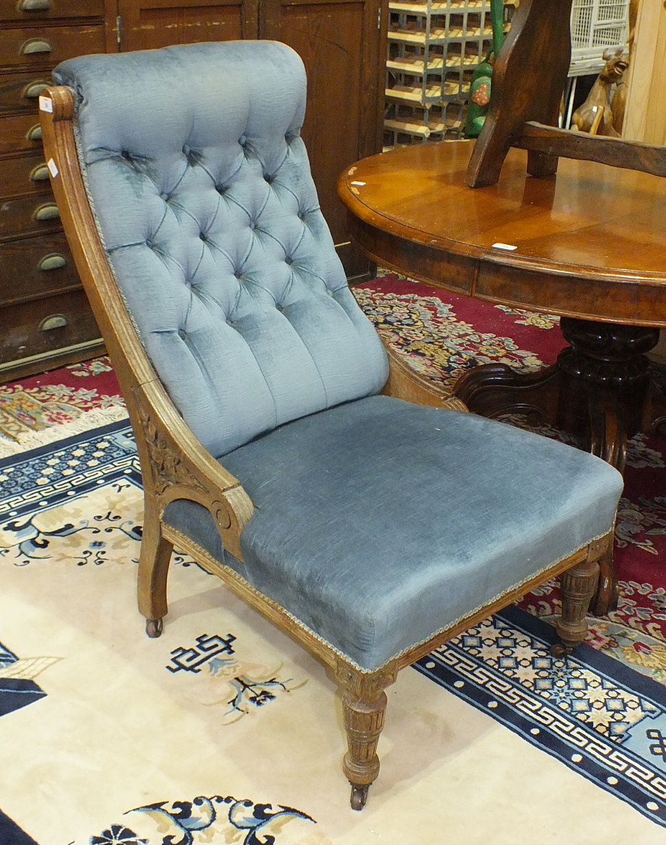 A Late-Victorian oak-framed upholstered button-back salon chair on reeded front legs.