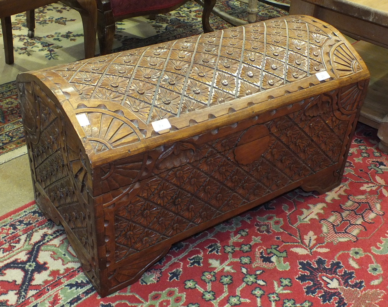 A teak domed-top chest carved overall with stylised flowers and sun bursts on the corners, 80cm