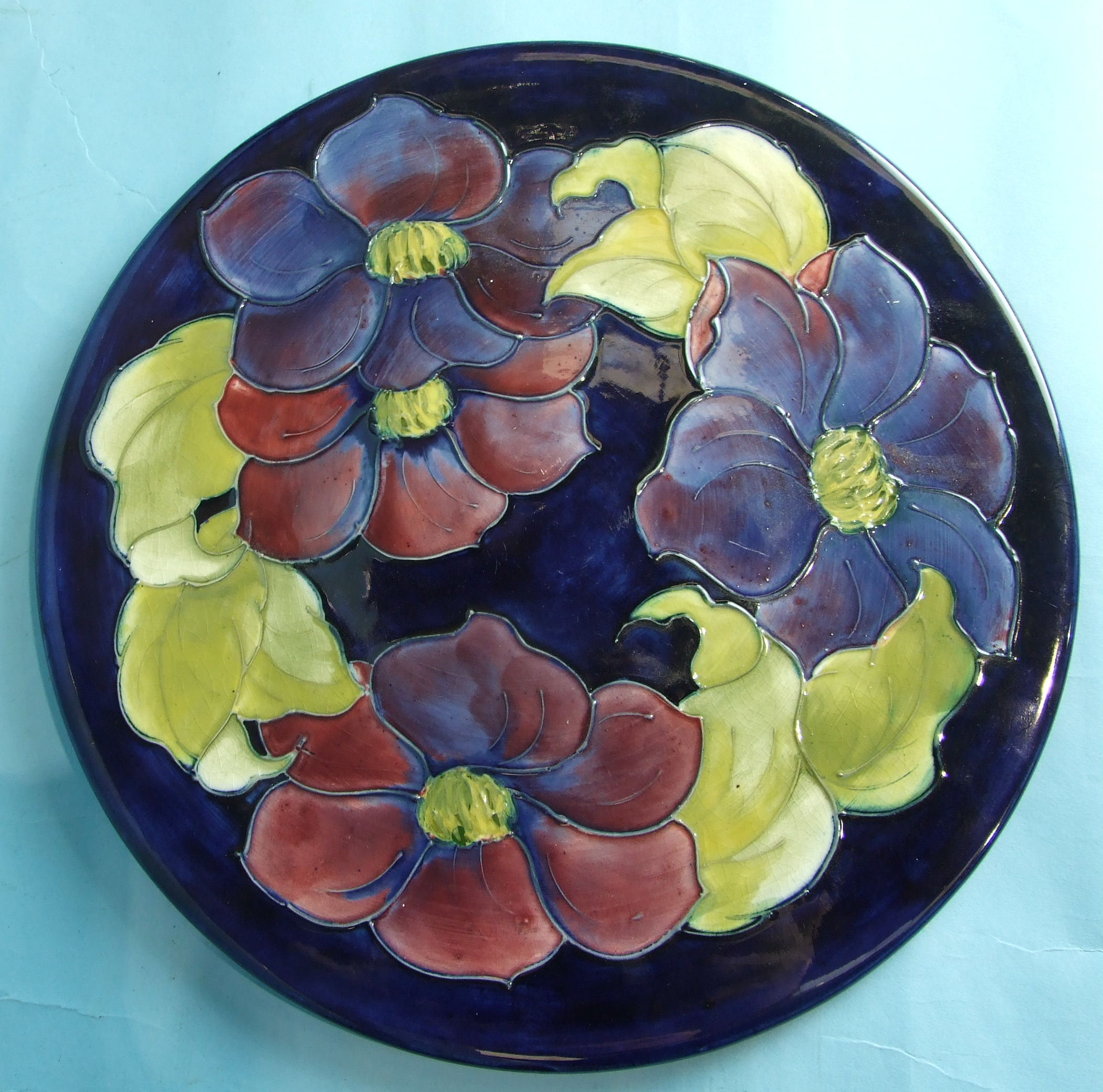 A Moorcroft circular plate decorated with clematis on a blue ground, with WM initials and