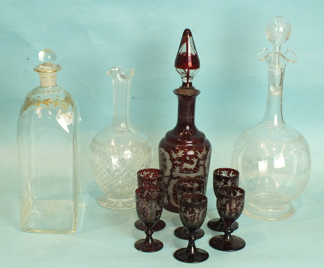 A 19th century red overlay glass liqueur set, (wrong stopper) and three glass decanters with