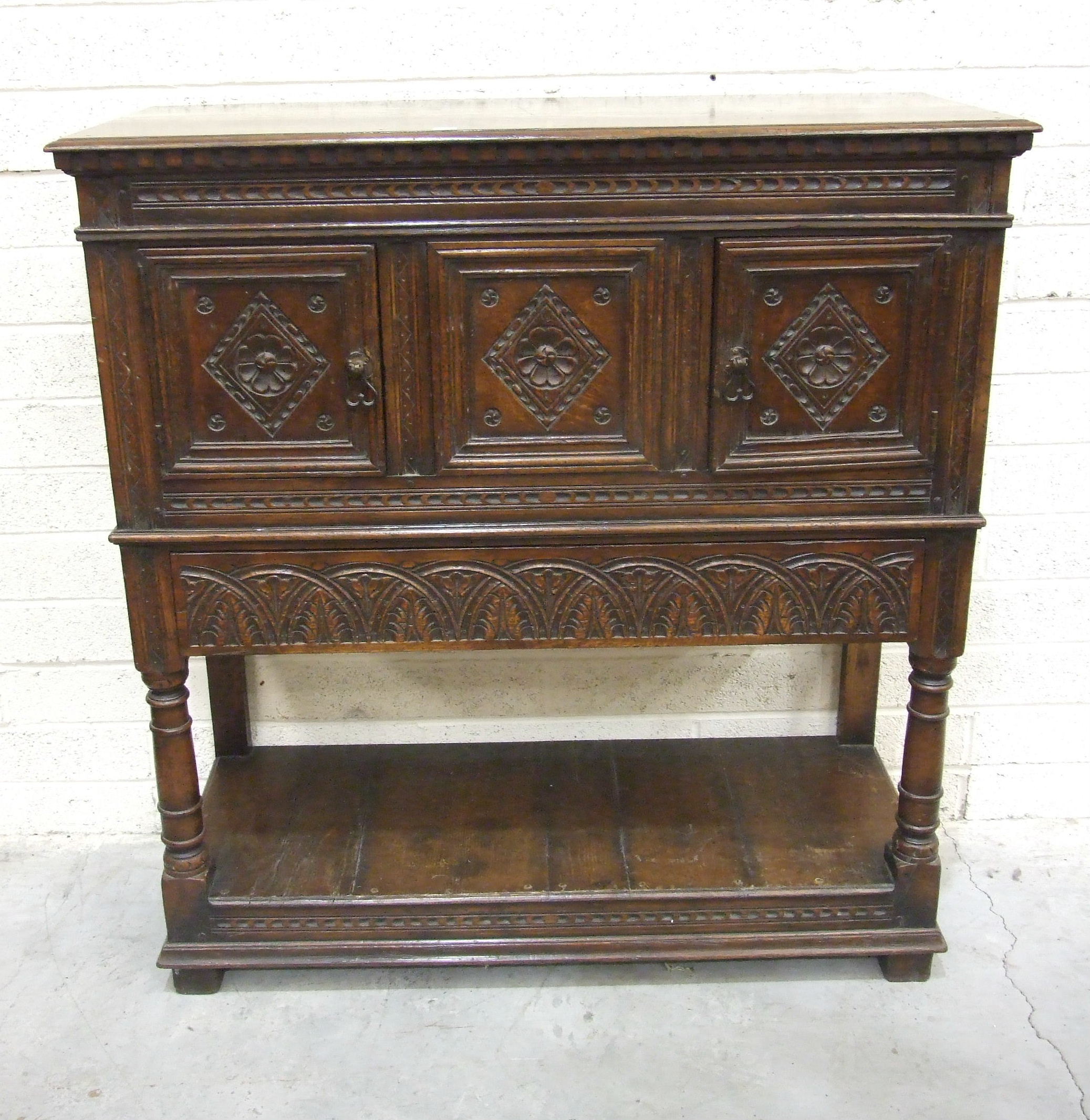 A reproduction oak court cupboard in the Tudor style, having a central Tudor rose carved panel,