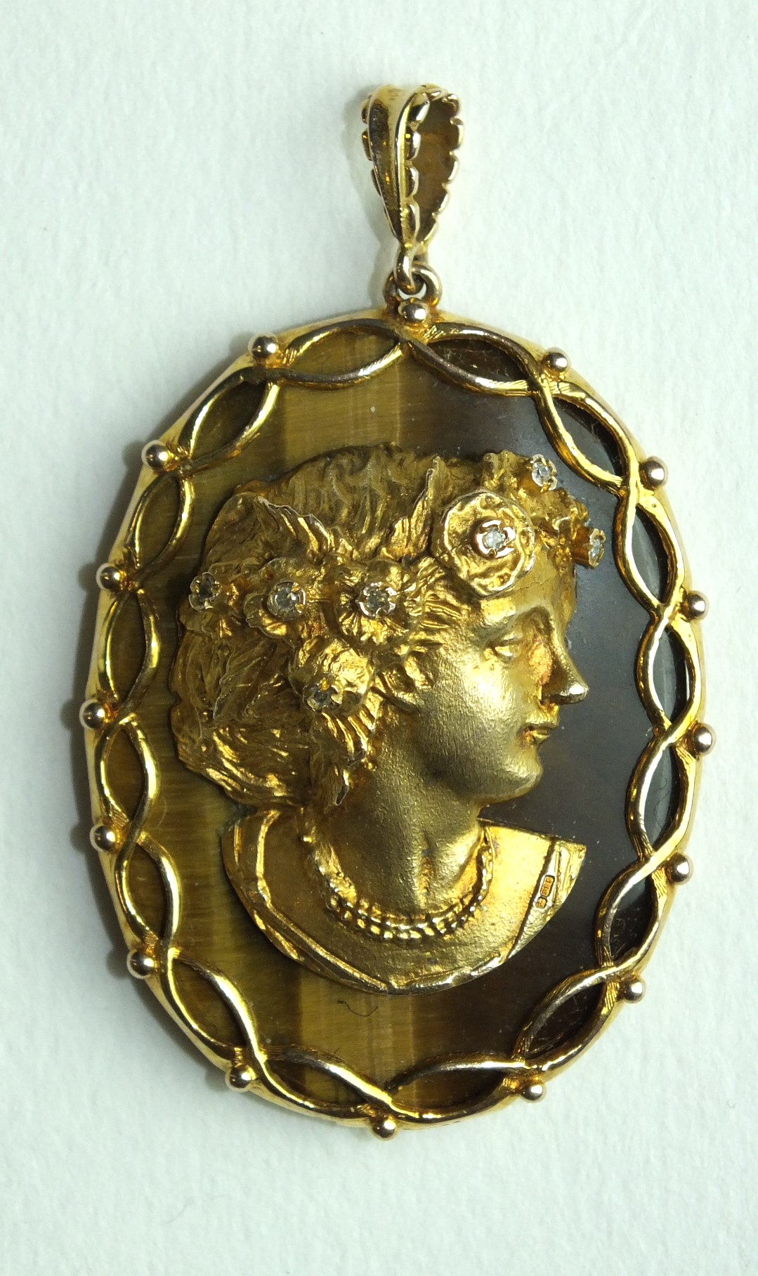 A large oval tiger's eye pendant overlaid with a gold profile in high relief of a young woman with