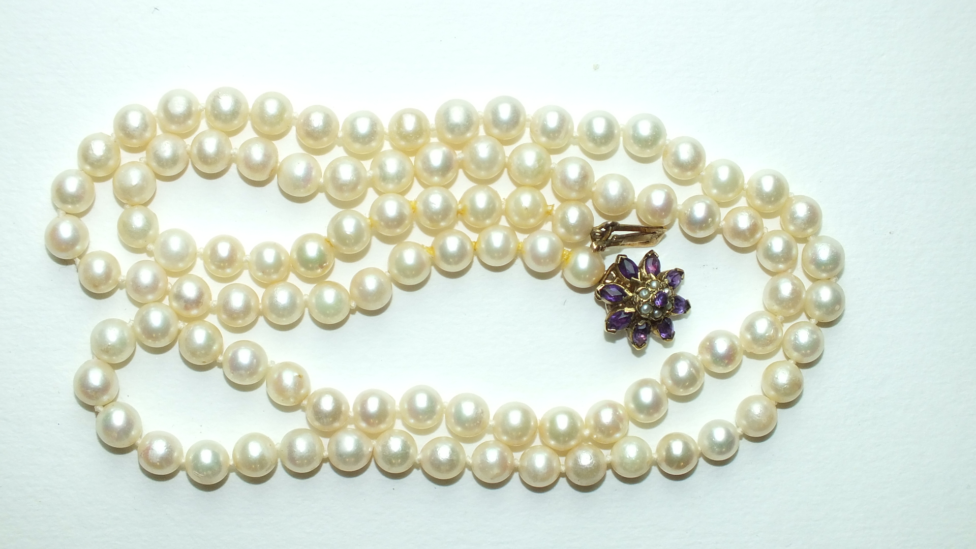 A long string of 95 uniform cultured pearls, 7mm diameter, with 9ct gold clasp set amethyst and seed