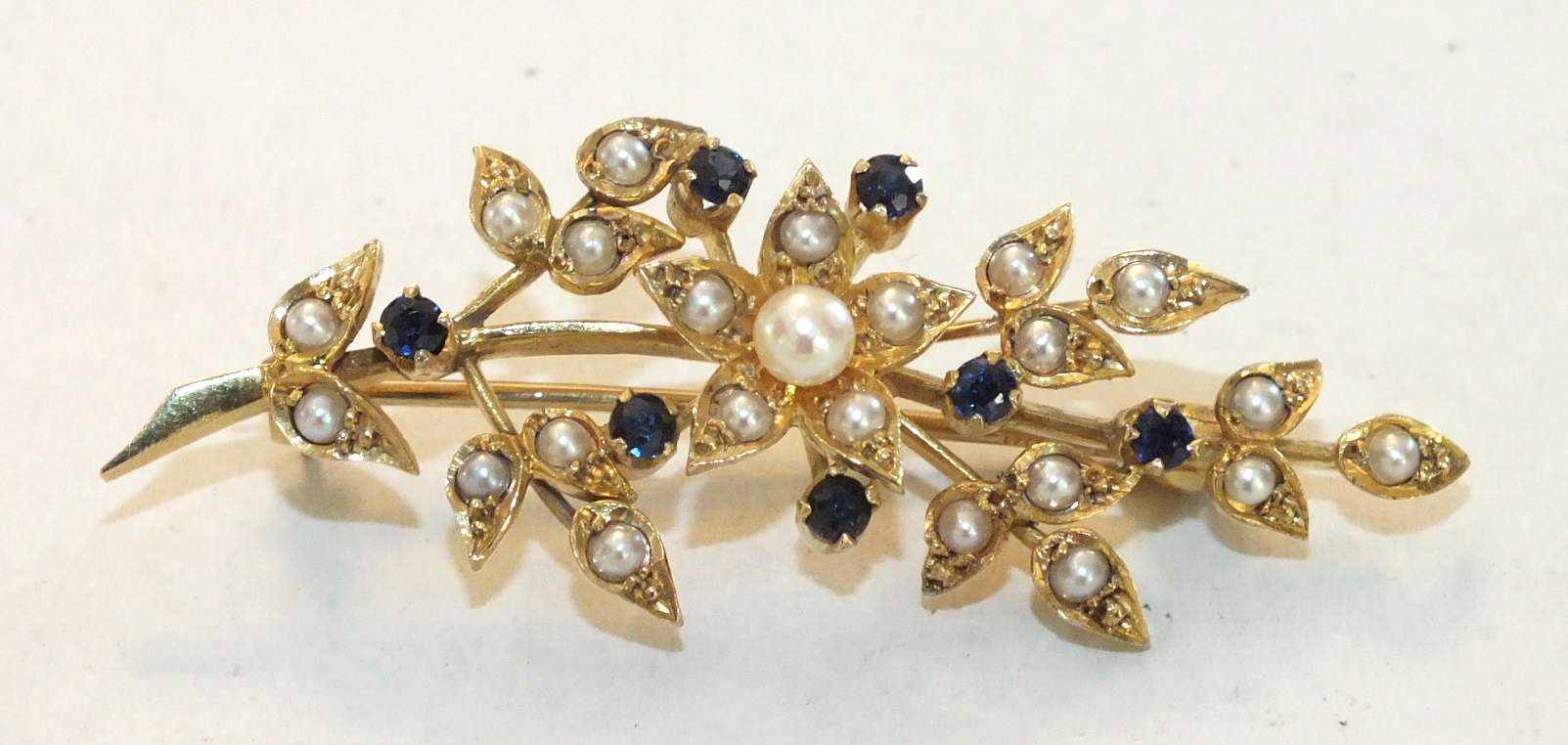 A sapphire and pearl spray brooch claw-set seven round-cut sapphires, amongst demi-pearl-set leaves,