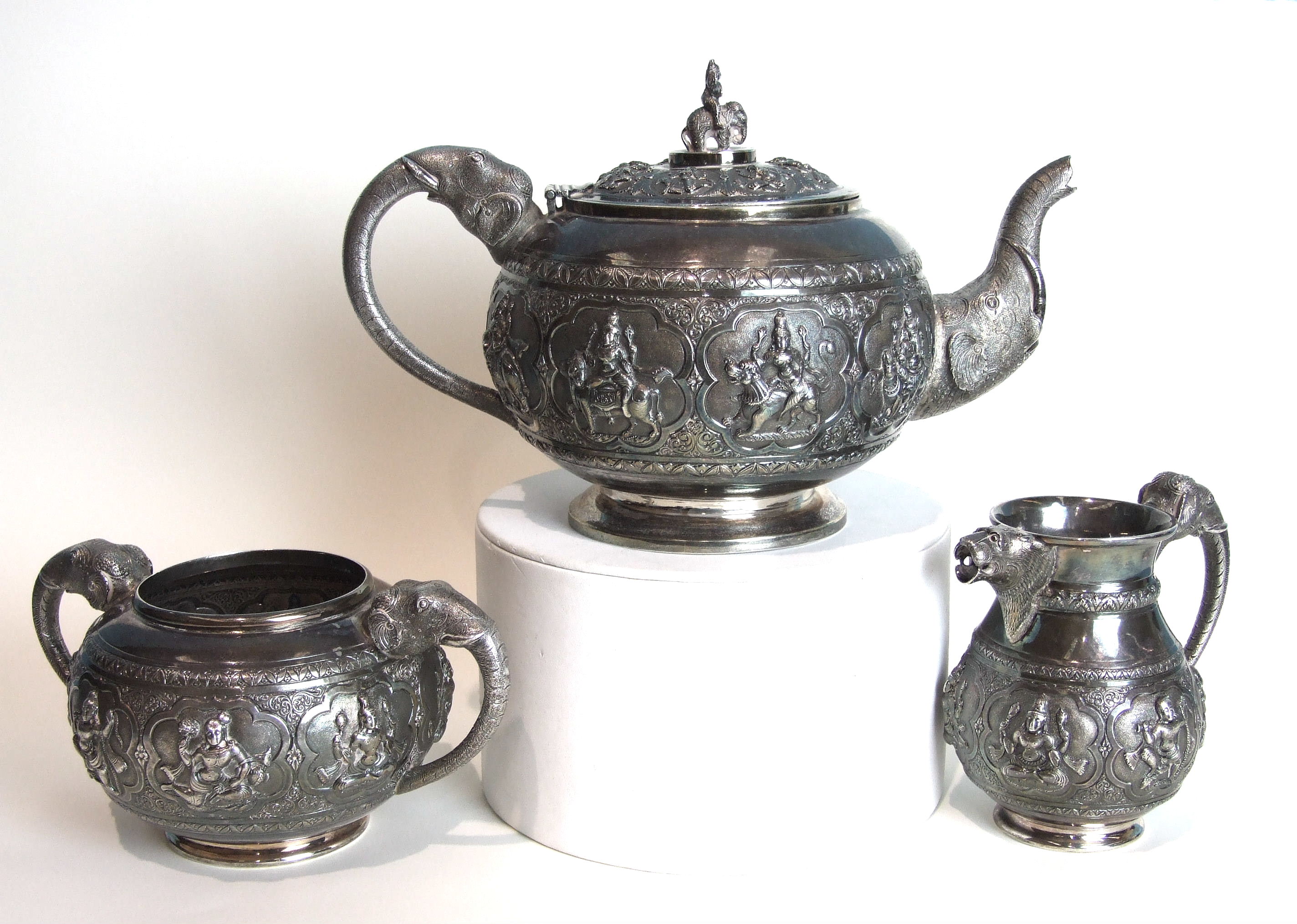 An Indian silver three-piece tea service of circular compressed form, heavily-embossed with panels