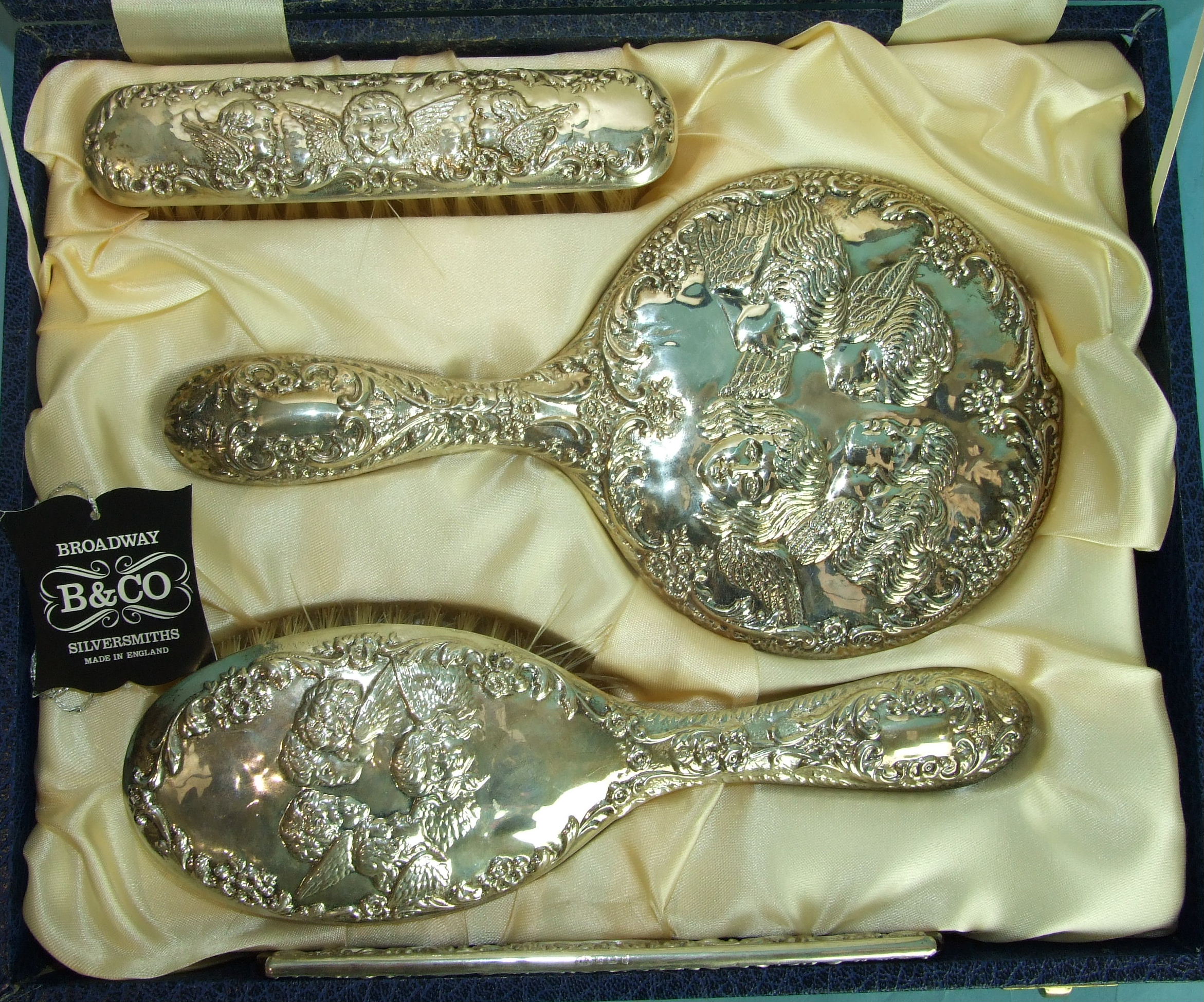 A reproduction silver dressing table set embossed with winged cherubs, in fitted case.