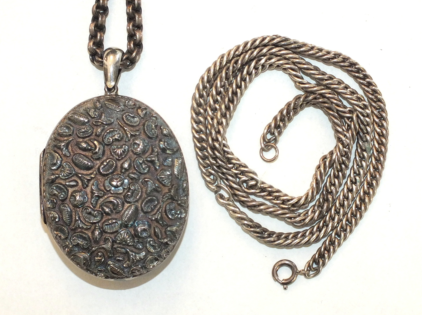 A large white metal locket embossed on both sides with flowers, leaves and shells, and two