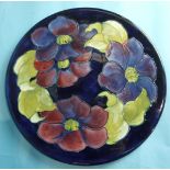 A Moorcroft circular plate decorated with clematis on a blue ground, with WM initials and