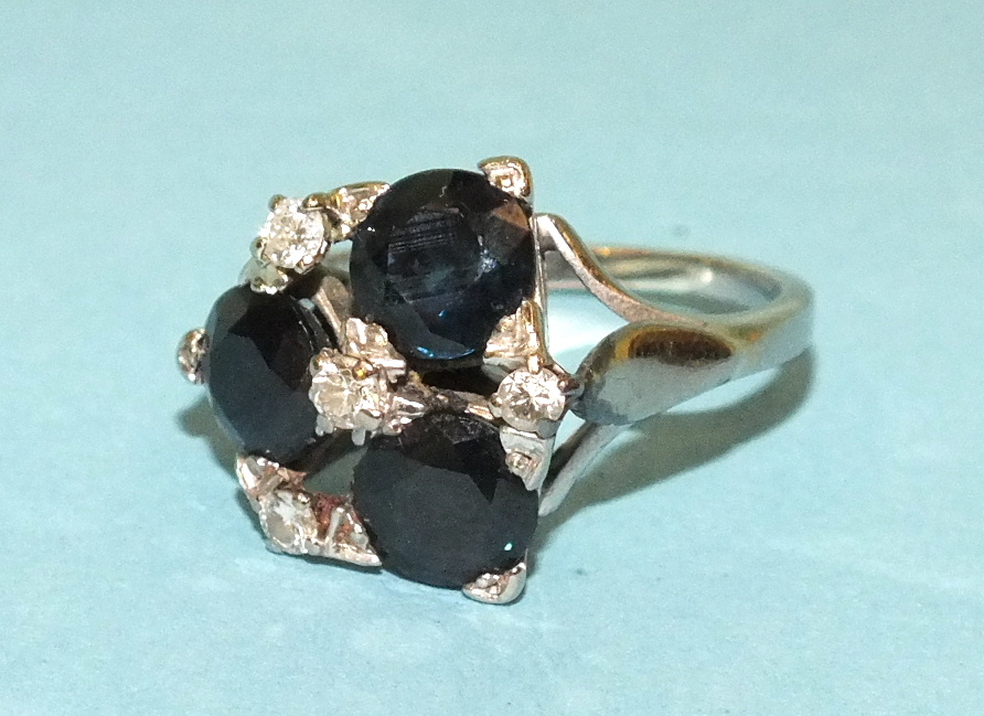 A sapphire and diamond ring claw-set a cluster of three round-cut sapphires, with diamond points