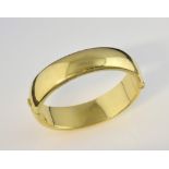 Oval hinged bangle, measuring 1.7cm wide, with hidden clasp, in yellow metal stamped 18 ct. weight