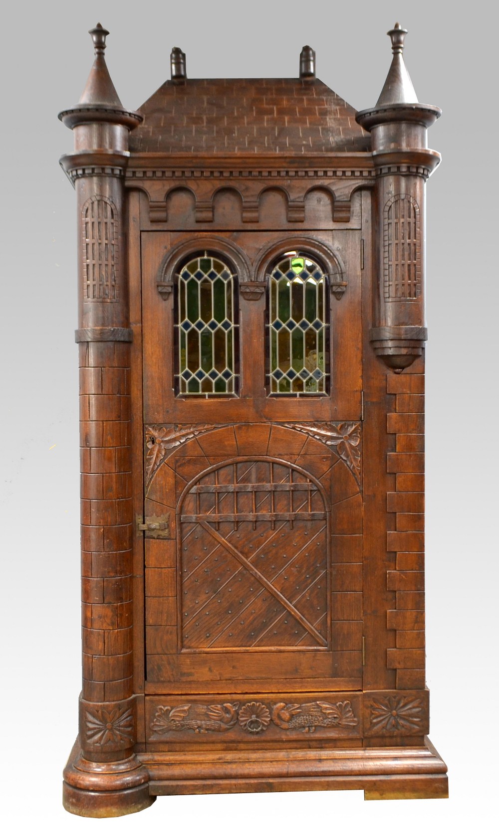 German oak single door cabinet with pitched top and turrets, arched windows with stained glass,