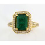 Emerald and diamond set ring, the step cut stone of vibrant colour in claw setting within a border