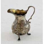 George II silver cream jug with embossed decoration, scroll handle, on three pad feet, by John