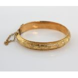 Early 20th C babies oval hinged bangle, with floral engraving and safety chain, in yellow metal