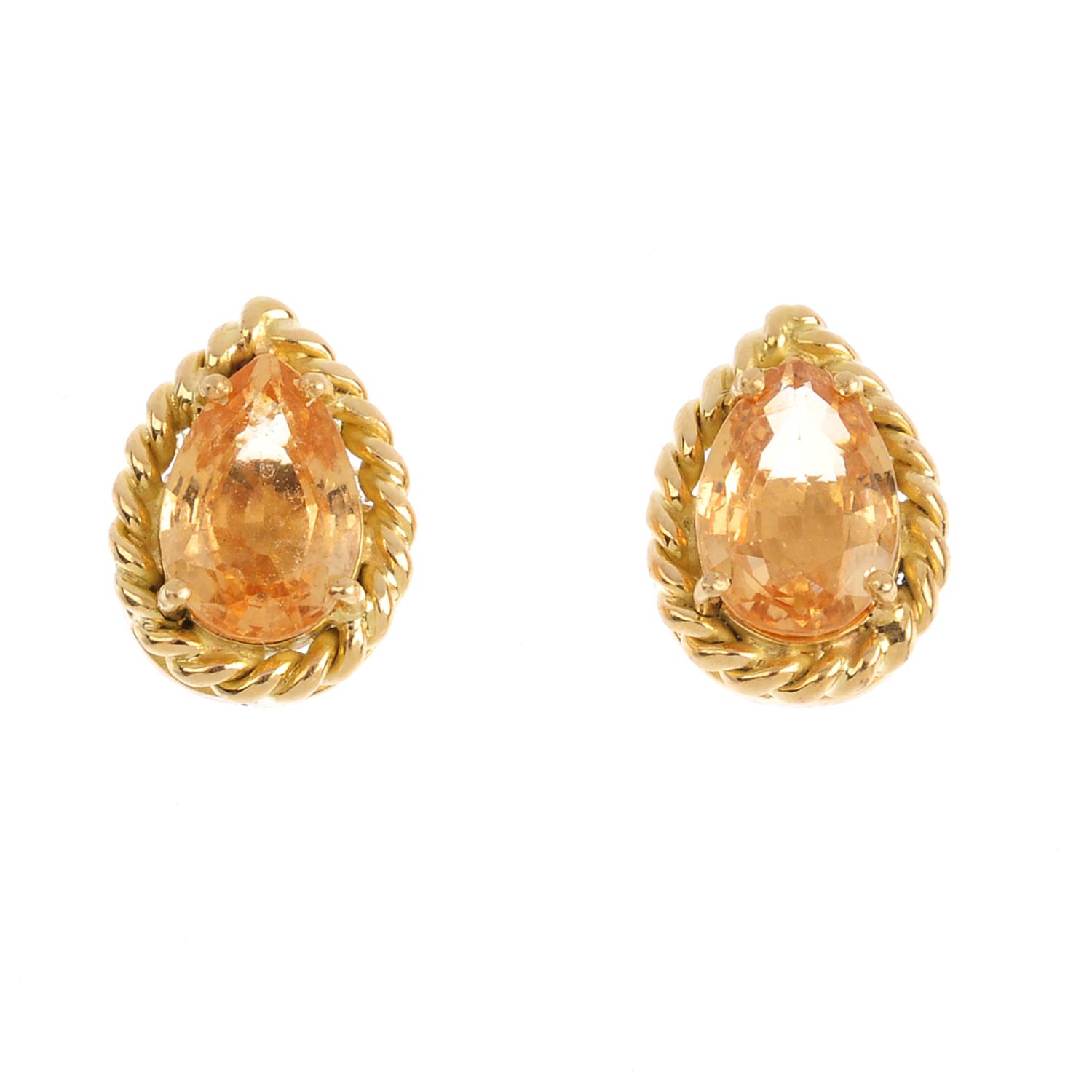 A pair of garnet stud earrings. Each designed as a pear-shape orange garnet, within a rope-twist