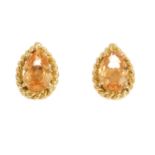 A pair of garnet stud earrings. Each designed as a pear-shape orange garnet, within a rope-twist