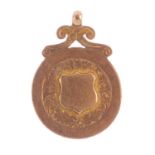 An early 20th century 9ct gold fob. Designed as an embossed shield, within a foliate panel border,