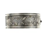 A late Victorian silver hinged bangle. To the half-bangle a raised border with applied flowers and