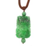 A carved jade pendant. The brown woven cord, with jade bead detail, suspending a rectangular jade