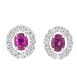 A pair of ruby and diamond cluster earrings. Each designed as an oval-shape ruby, with brilliant-cut