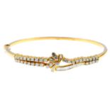 An 18ct gold diamond hinged bangle. Of openwork design, the baguette and brilliant-cut diamond