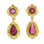 A pair of garnet earrings. Each designed as a pear-shape garnet, within a textured scrolling