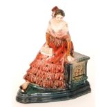 A 1920s model of a Spanish lady dressed in red with flowers in her hair perched on a solid seat,