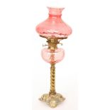 A Victorian brass oil lamp with cast foliate base and cranberry reservoir and shade,