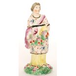 An early 19th Century Staffordshire figure of a lady stood in a floral dress and yellow underskirt