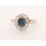 An 18ct sapphire and diamond cluster ring, oval cut sapphire with a twelve diamond surround,