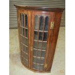 A George III mahogany bowfronted hanging corner cupboard enclosed by a pair of lancet bar glazed