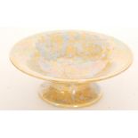 A small Ruskin Pottery footed bowl decorated with a mottled blue over the ochre lustre ground,