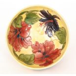 A Moorcroft footed bowl decorated in the Hibiscus pattern with tubelined flowers against a yellow